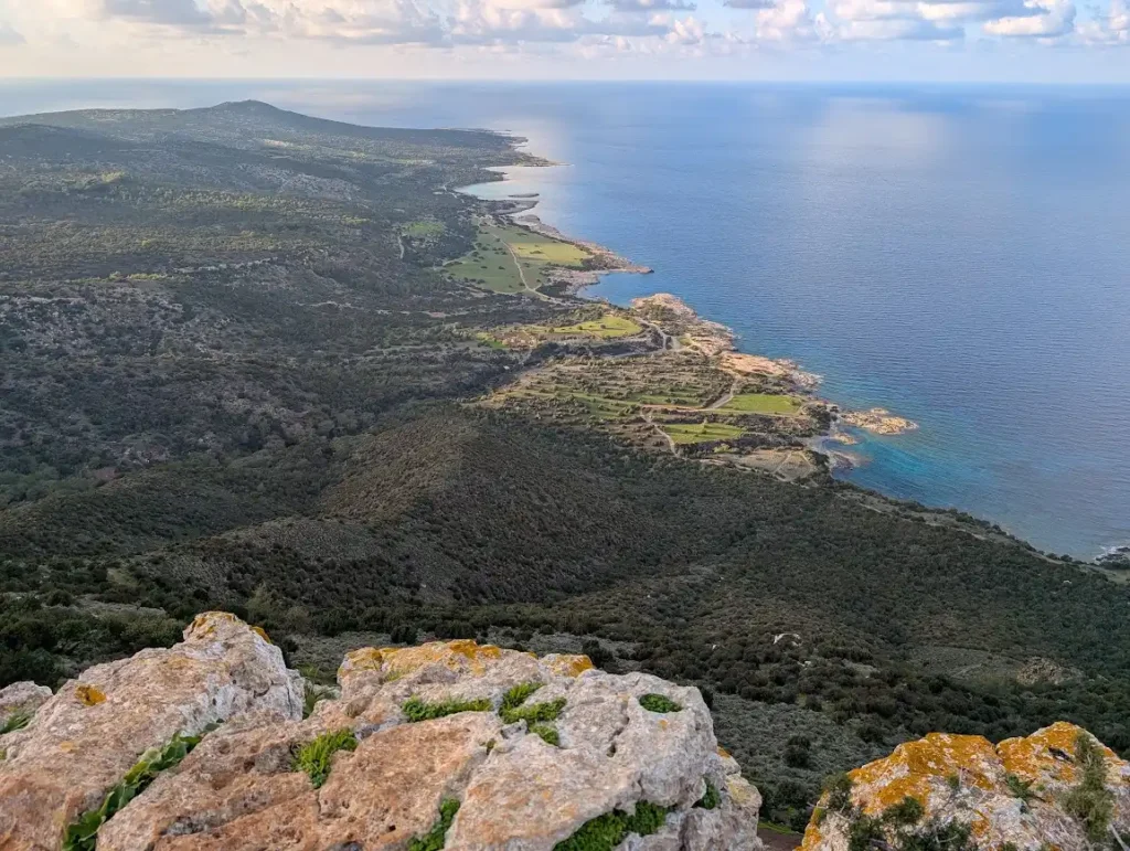 A wide-angle aerial view of the rugged Akamas Peninsula coastline in Cyprus, showing the transition from forested hills to the Mediterranean Sea.