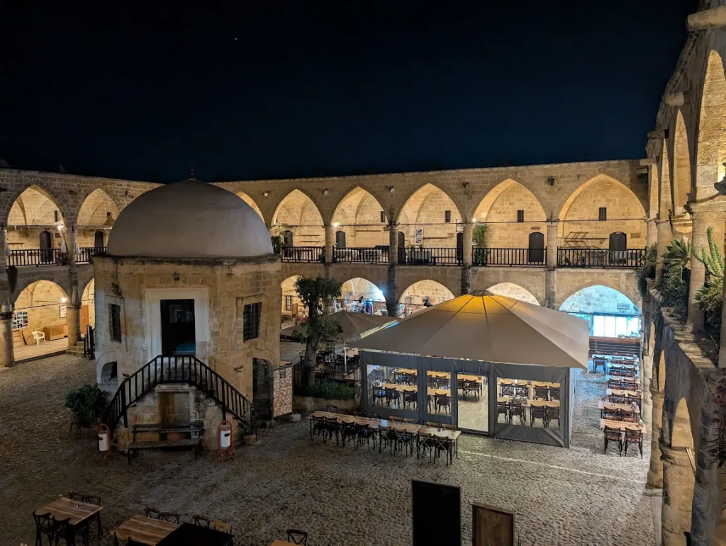 Büyük Han Ottoman caravanserai courtyard at night in northern Nicosia, Turkish side of Cyprus, with lit arches and outdoor seating, January 2025.
