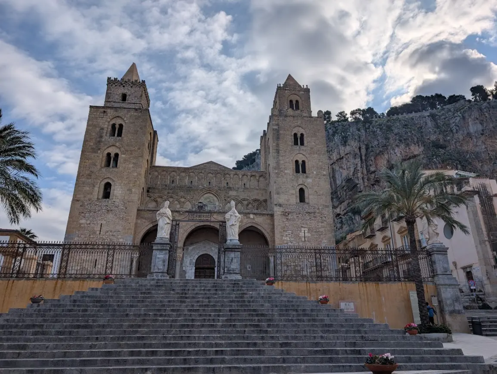 Norman cathedral in Cefalù, Sicily, with twin towers set against a dramatic rock face backdrop