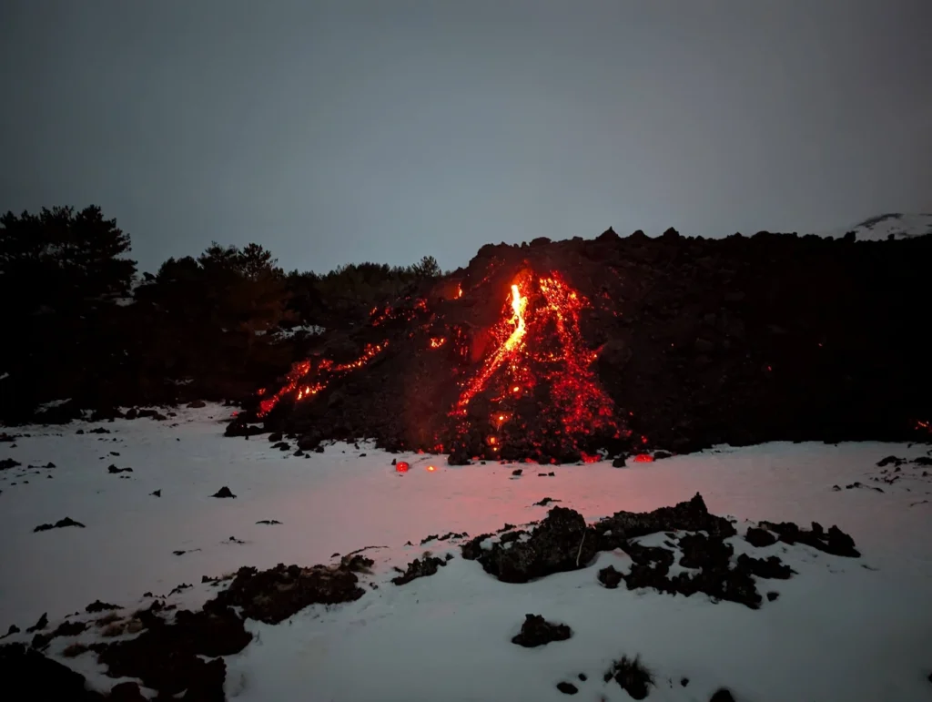 Night view of active lava flow on Mount Etna, Sicily, during winter with snow on the ground.