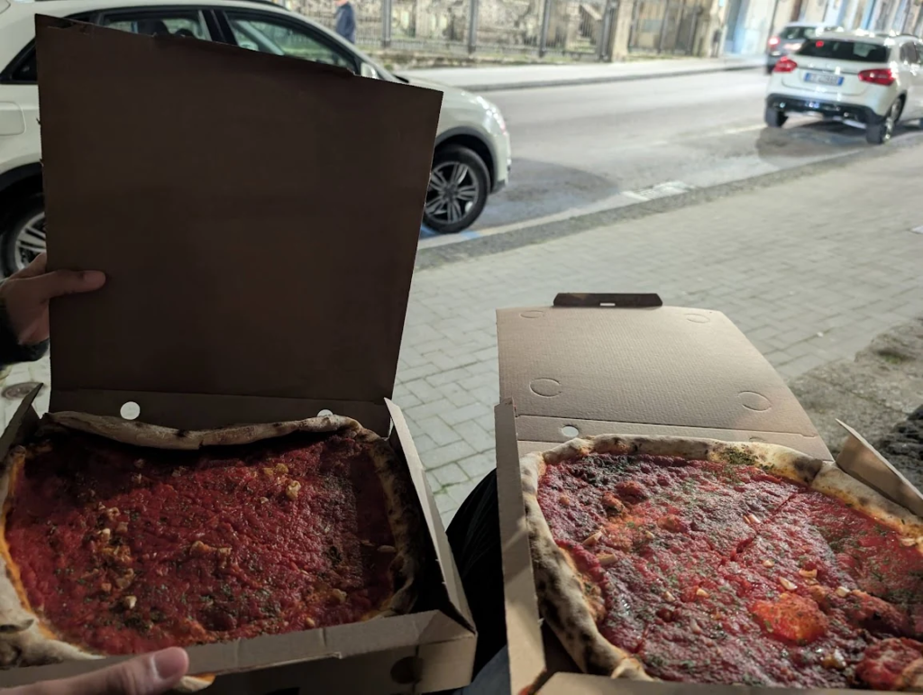 Two takeaway pizzas in cardboard boxes eaten on a street in Caltagirone, costing €5 each