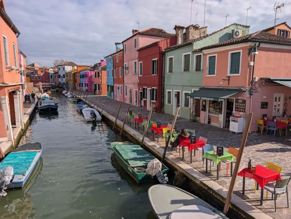 Canal lined with brightly painted houses and moored boats on Burano island, Venice, Italy