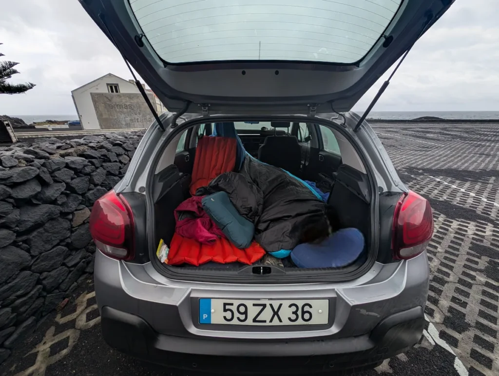 Open boot of a Citroën C3 rental car showing inflatable sleeping mats and sleeping bags, parked in São Miguel, Azores