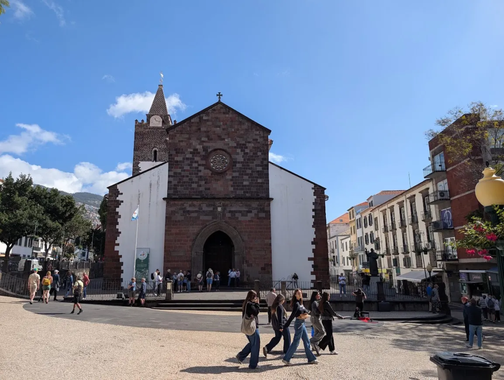 Funchal Cathedral with its dark stone facade, whitewashed walls and bell tower on a sunny day
