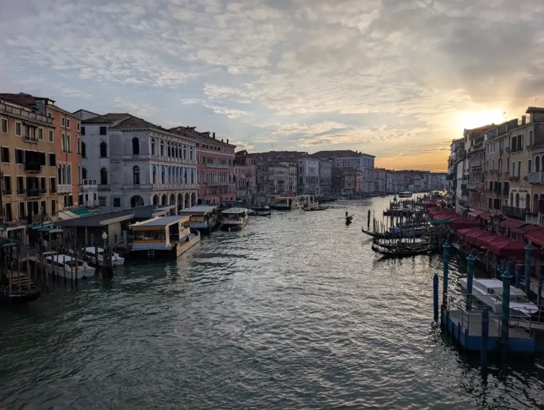 View of the Grand Canal at sunset from the Rialto Bridge, Venice, with gondolas, vaporetto stops, and historic palazzos lining both banks.