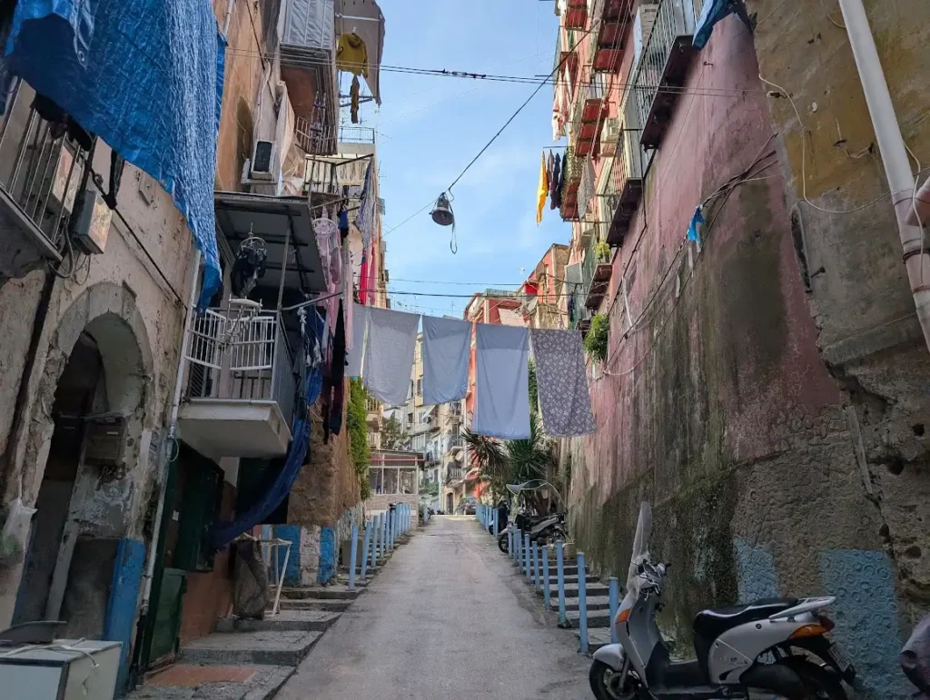 Narrow alley in Naples old town with laundry hanging between buildings and a scooter parked below, Italy