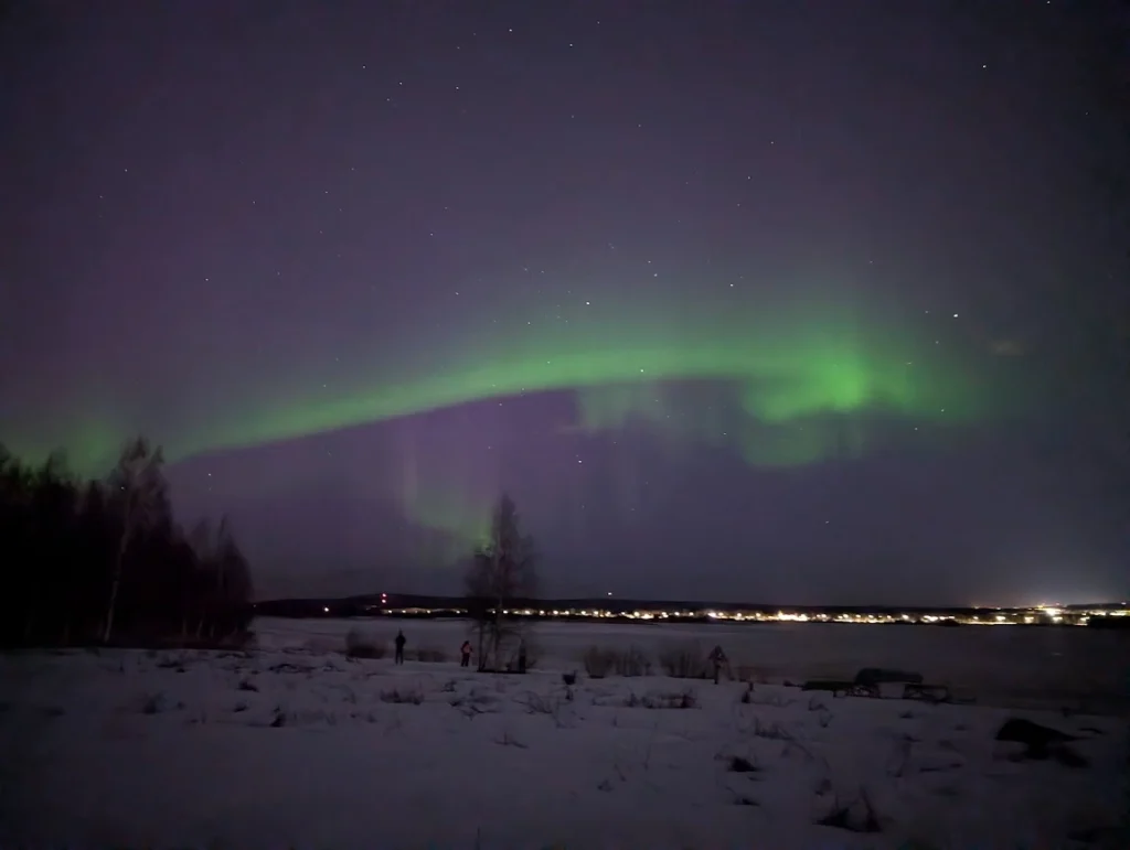 Northern lights arching over a frozen lake and snow-covered landscape at night, Rovaniemi, Finland