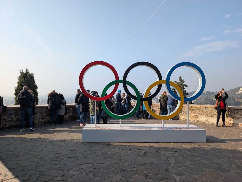 Olympic rings installation in Verona during the 2026 Winter Olympics with city views in the background