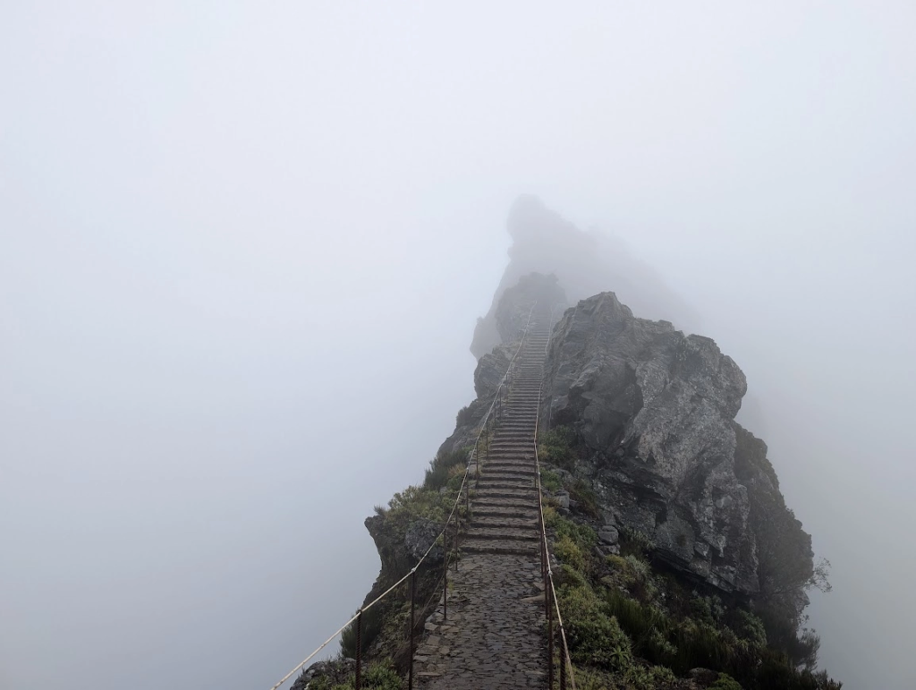 Stone staircase with rope railings climbing a rocky ridge into thick fog at Pedra Rija near Pico do Areeiro