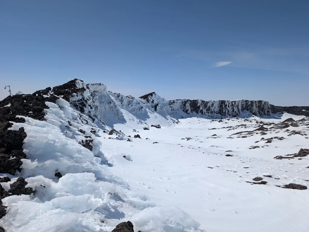 Snow-covered crater rim at the Pico summit with black lava rocks breaking through the ice, Pico, Azores