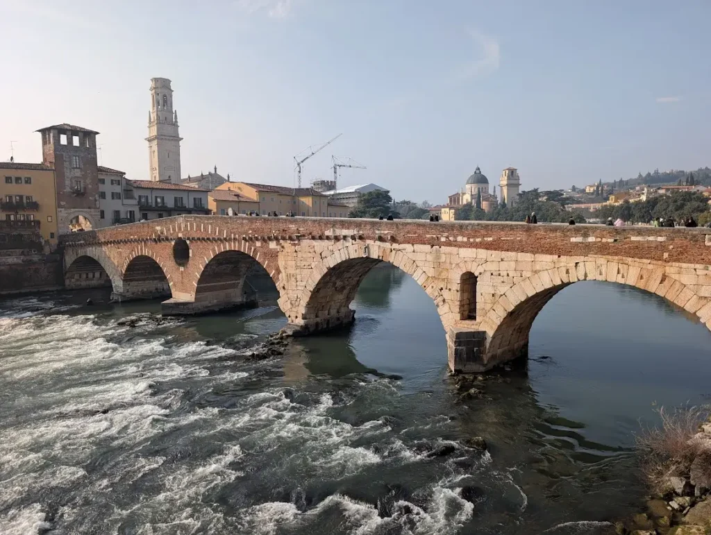 Roman Ponte Pietra bridge with stone arches over the fast-flowing Adige River, Verona cathedral tower in the background, Italy