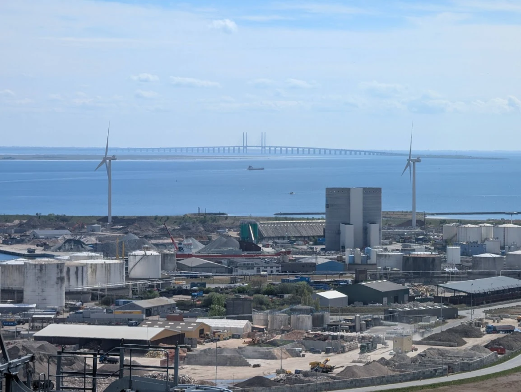 View from CopenHill in Copenhagen – industrial port in the foreground, Øresund Bridge connecting Denmark and Sweden visible in the distance