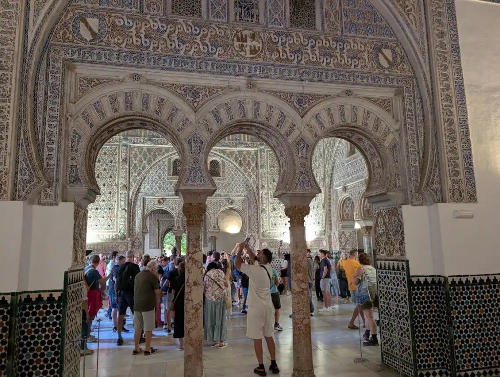 Crowded interior hall with Moorish arches and tilework inside the Royal Alcázar of Seville