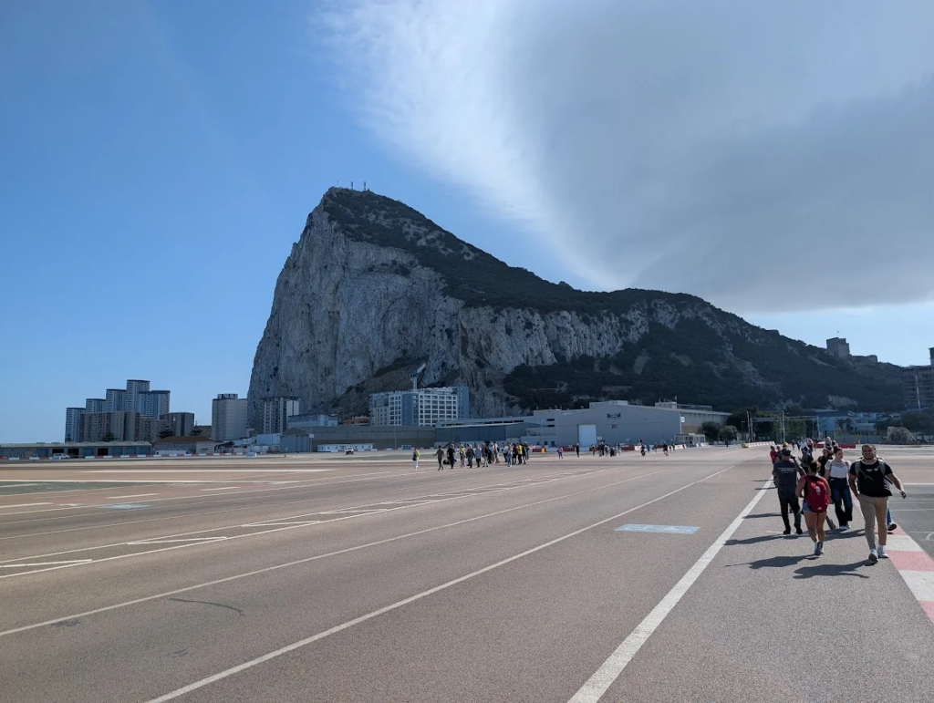 Pedestrians crossing Gibraltar airport runway on foot with the Rock of Gibraltar in the background