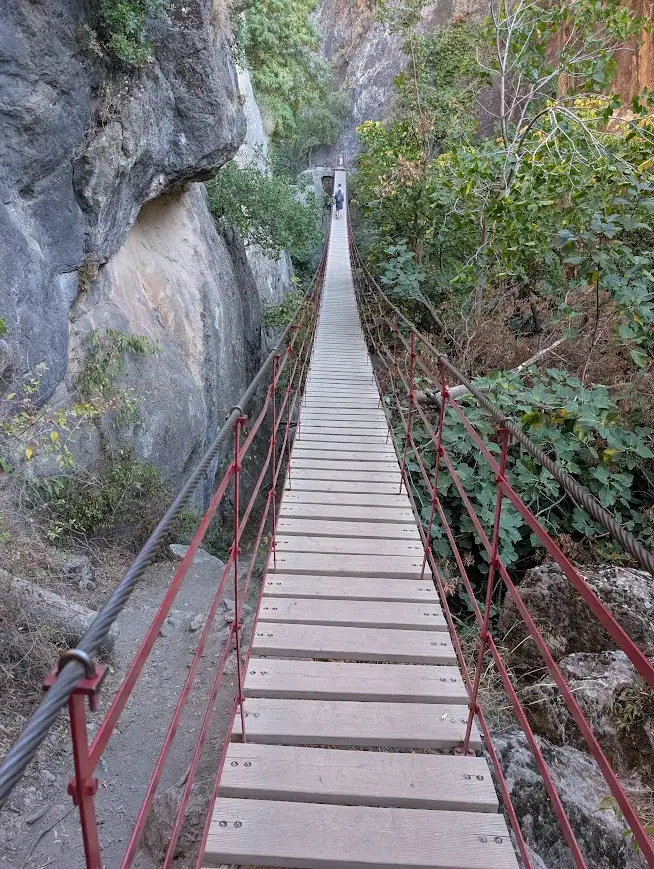Wooden plank suspension bridge with red railings crossing a gorge on the Los Cahorros trail, Sierra Nevada