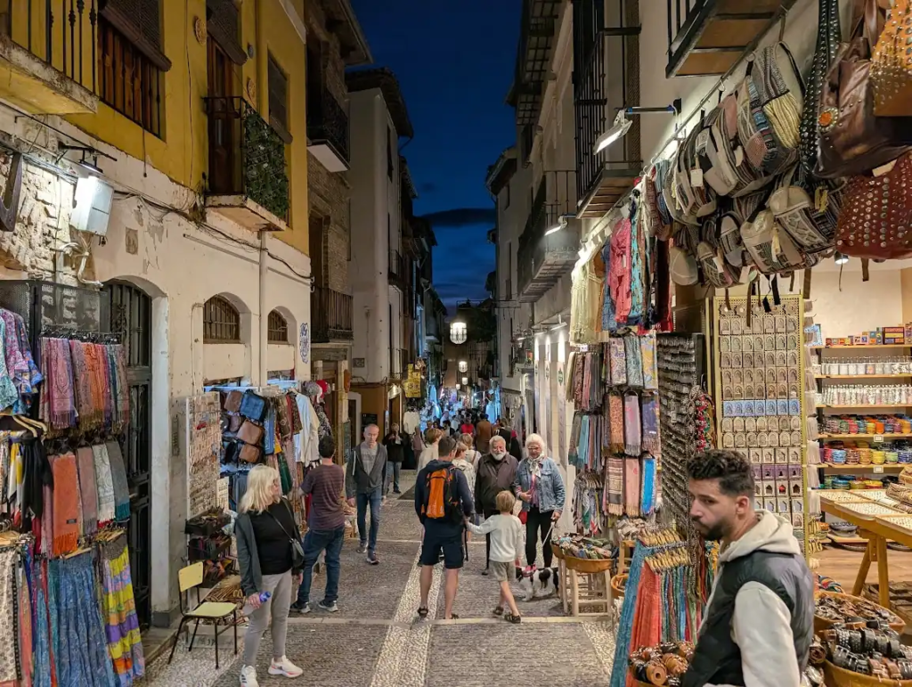 Narrow market street lined with textile and souvenir stalls at night in the Alcaicería, Granada