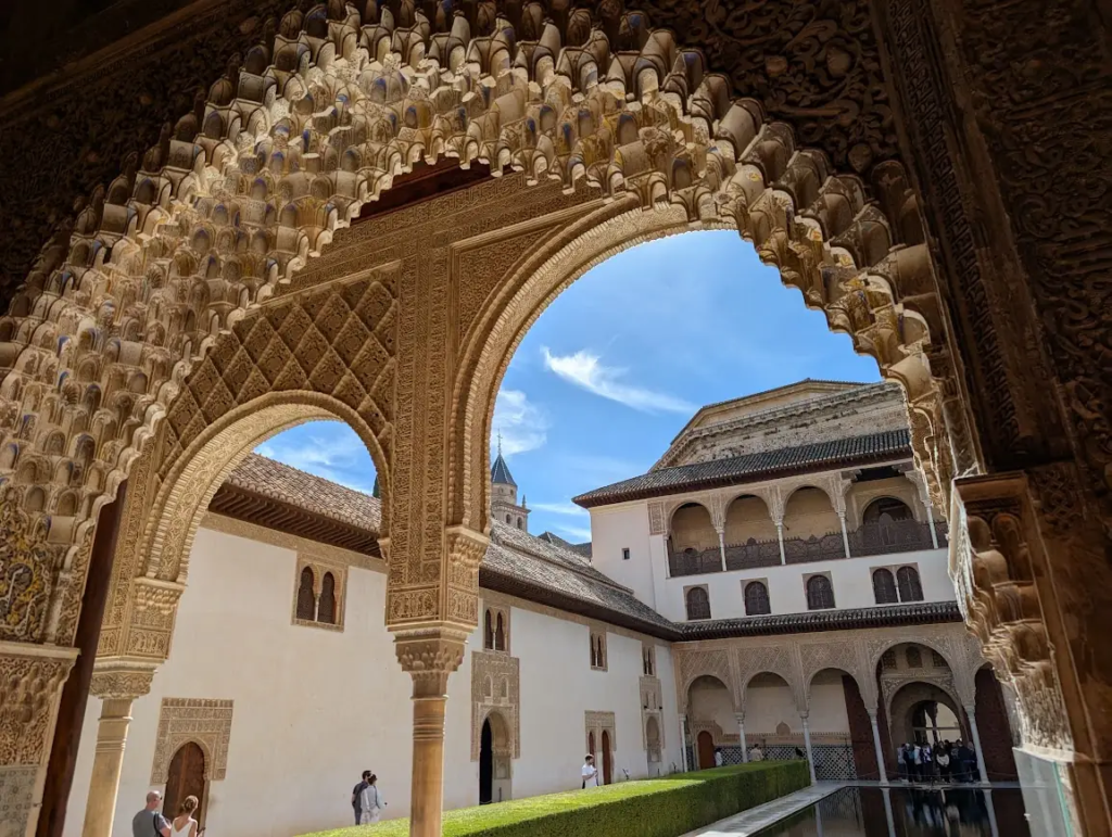 Ornate horseshoe arch framing a view of the Alhambra's Nasrid Palaces and courtyard pool, Granada