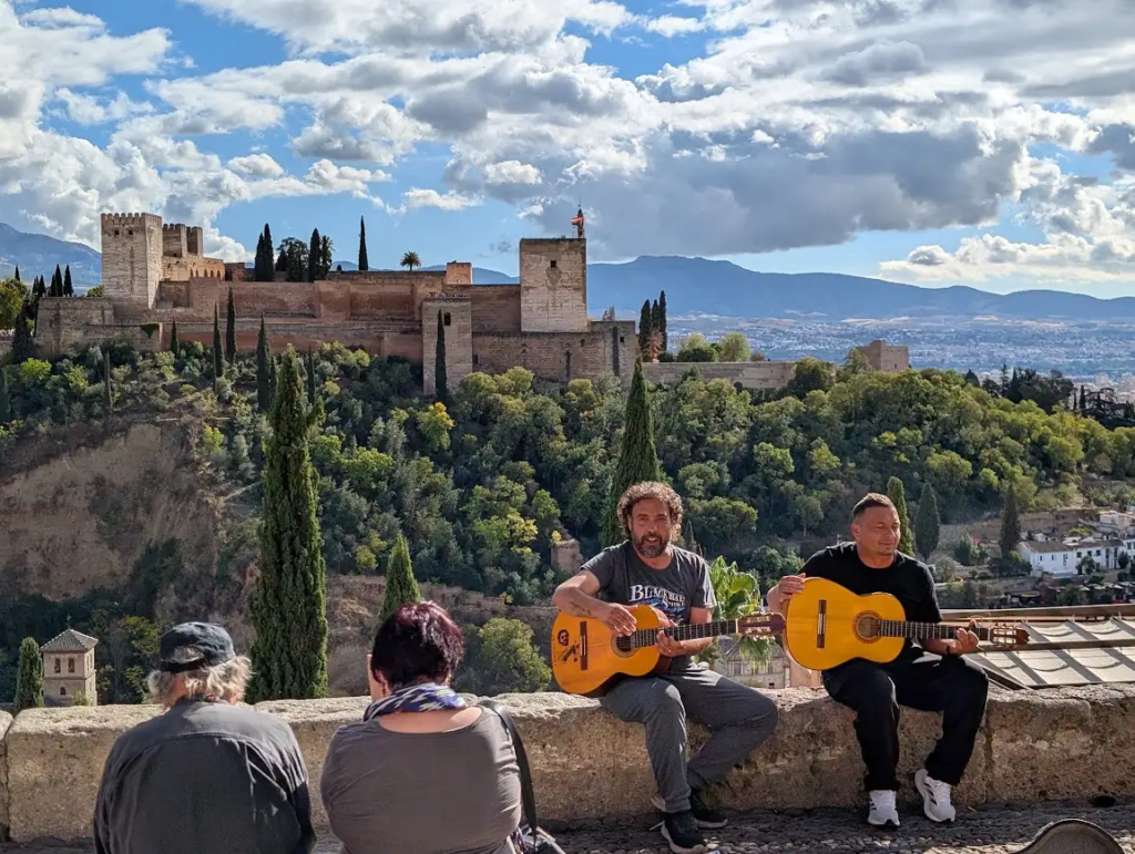 Two Gitano buskers playing guitar at Mirador de San Nicolás with the Alhambra and Sierra Nevada behind them, Granada