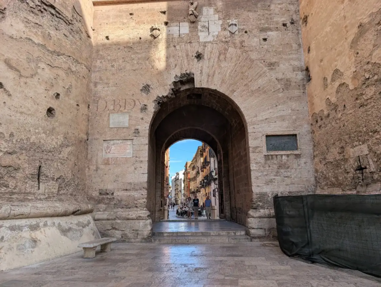 Stone archway of a historic city gate in Valencia's old town, Spain, with pedestrians walking through