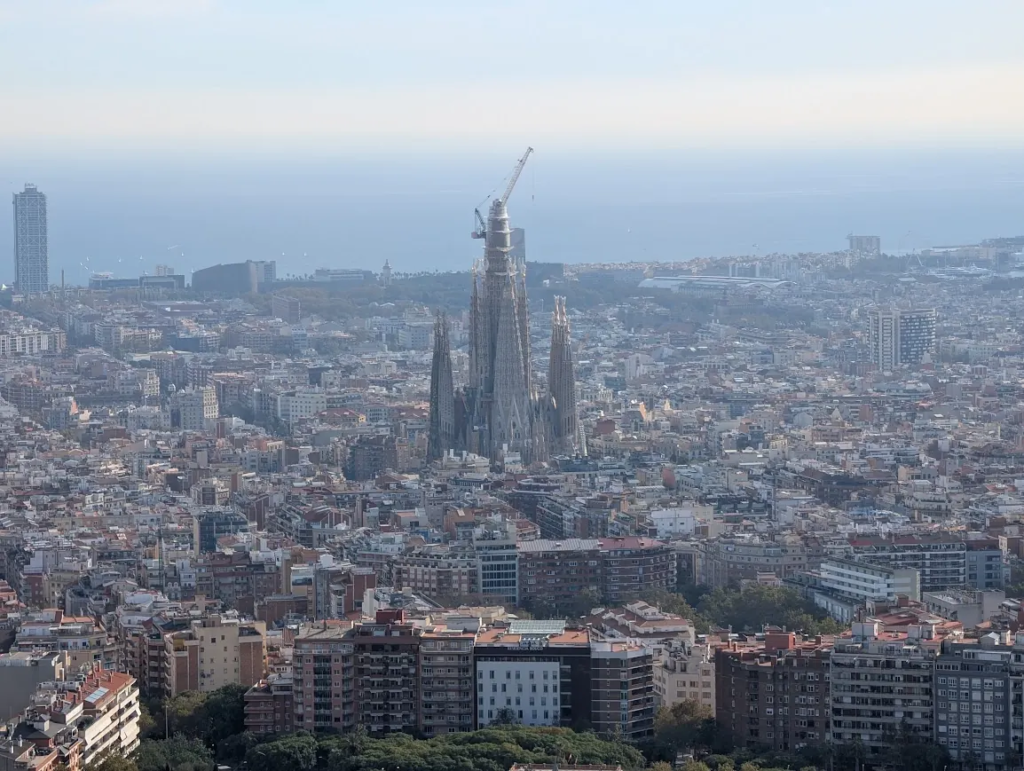 Aerial view of Barcelona skyline with the Sagrada Familia towers rising above the dense city grid, Mediterranean coast in the background
