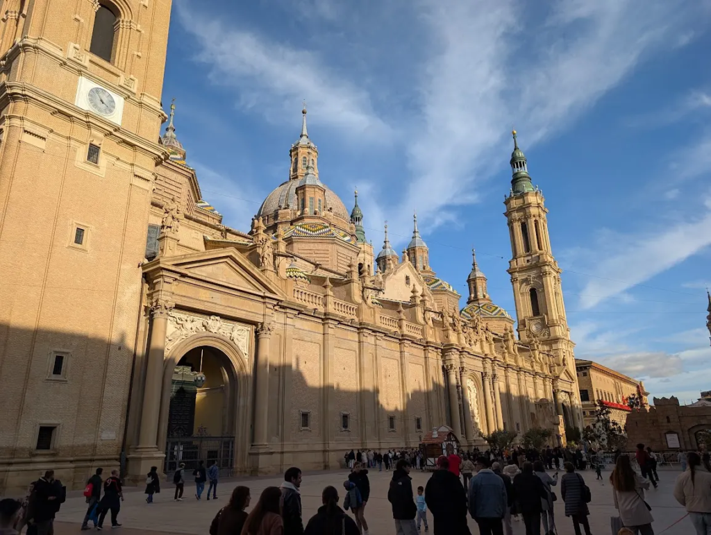 Basilica de Nuestra Senora del Pilar in Zaragoza, Spain, with tiled domes and towers above a busy plaza in late afternoon