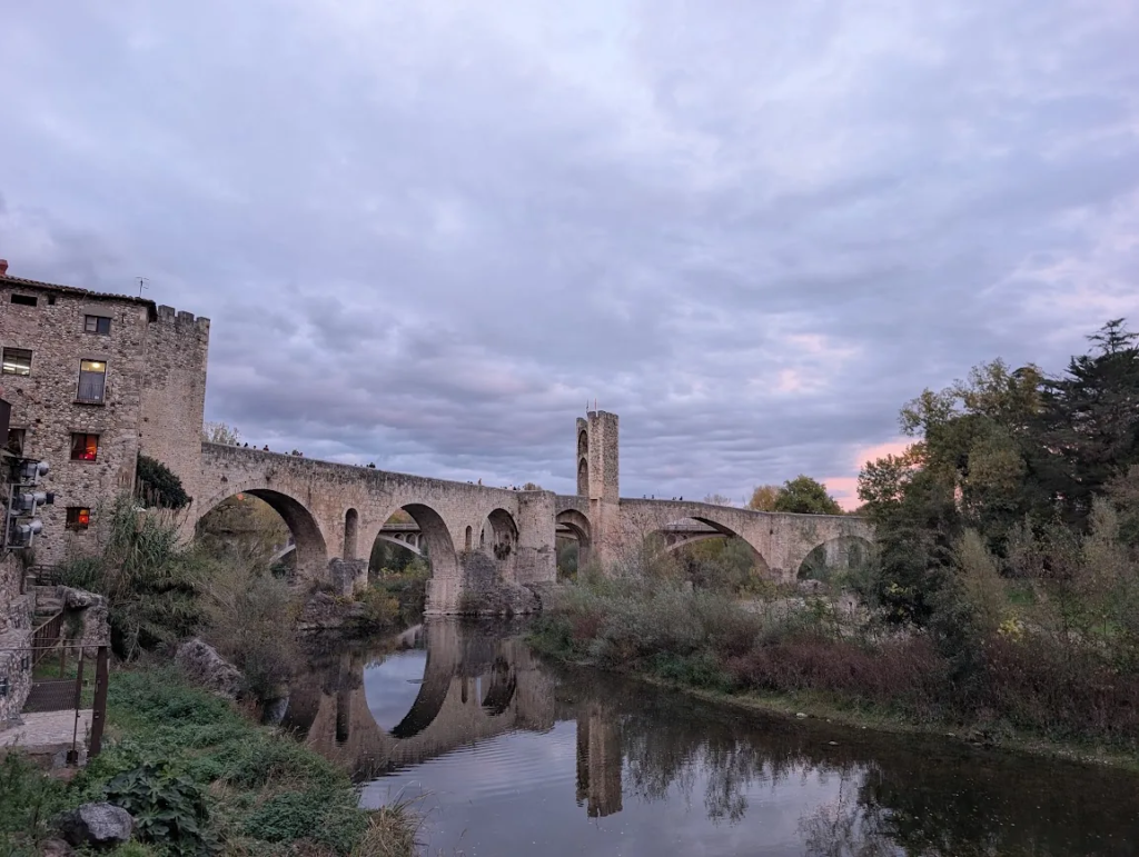 Medieval Romanesque stone bridge in Besalú, Catalonia, reflected in the river at dusk with the old town beside it