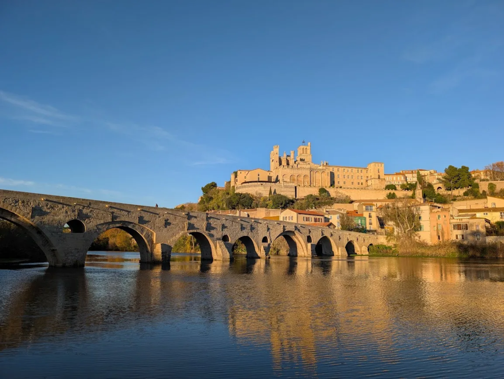 Medieval stone arch bridge Pont Vieux over the river in Béziers with the cathedral on the hill above in evening light