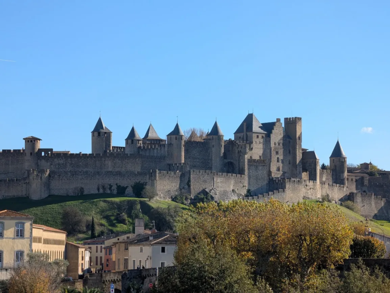 Fortified medieval city of Carcassonne in southern France, with its double walls and conical towers above autumn trees on a clear November day