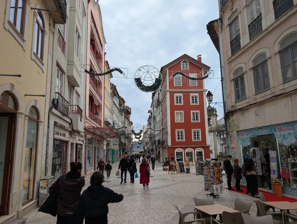 Pedestrian shopping street in Coimbra, Portugal, with a red building and Christmas decorations overhead