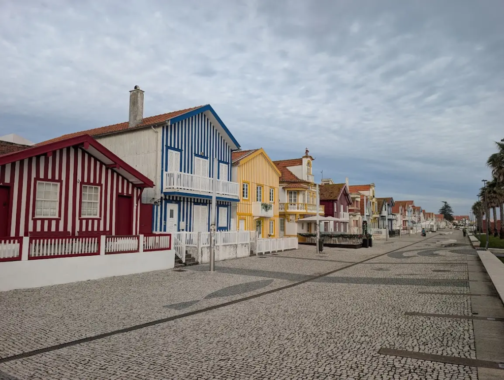 Row of red, blue and yellow striped beach houses on a cobblestone promenade in Costa Nova near Aveiro, Portugal