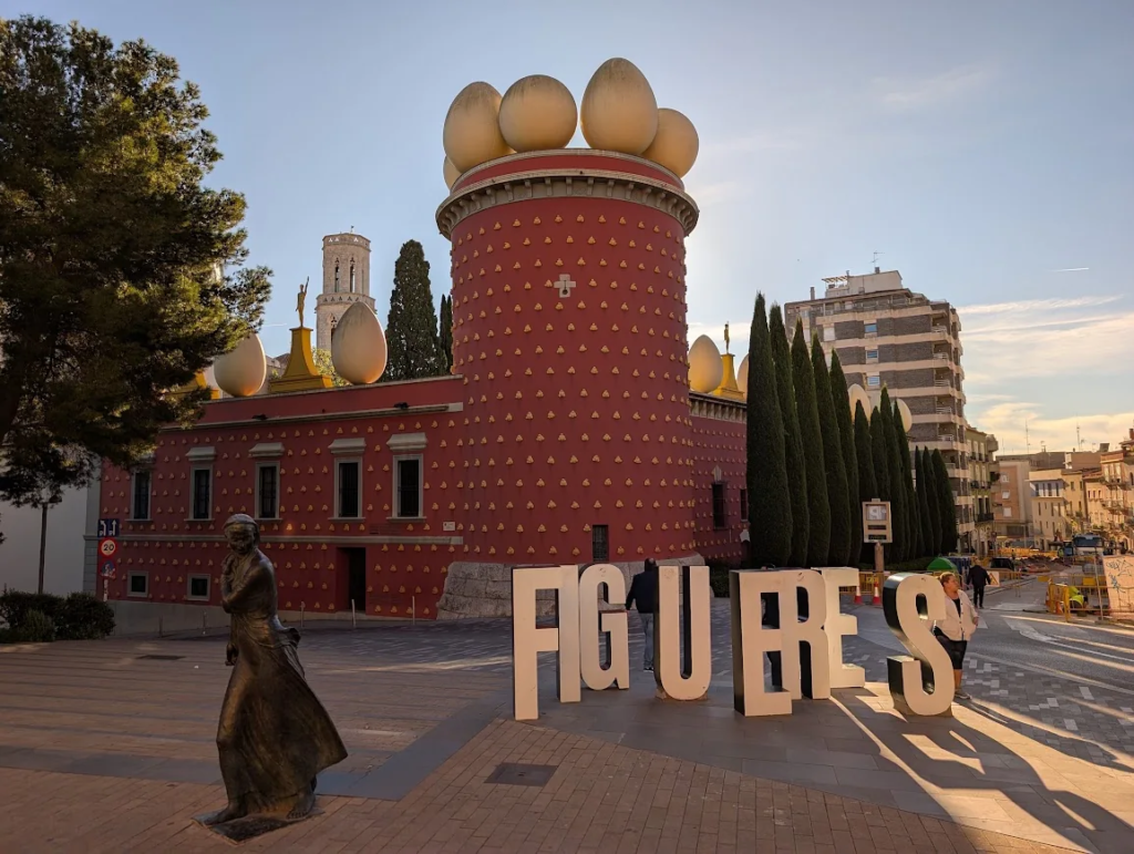 Dalí Theatre-Museum in Figueres, red facade with giant egg sculptures on the roofline, FIGUERES letters sculpture in front