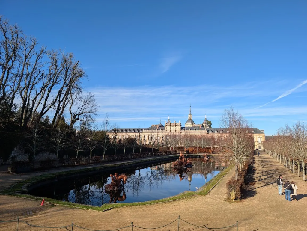 Royal Palace of La Granja de San Ildefonso in Spain, seen across a garden pond with bare winter trees and a clear blue sky