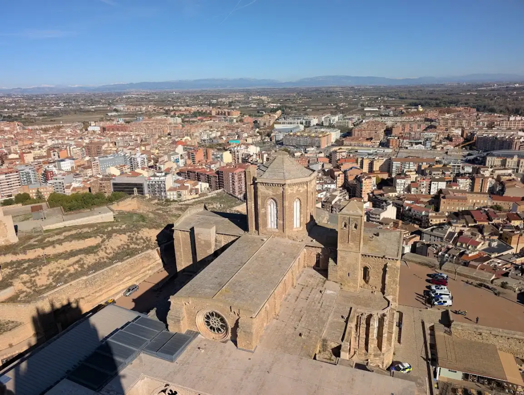 Aerial view of La Seu Vella cathedral in Lleida, Spain, with the modern city and distant mountains behind it