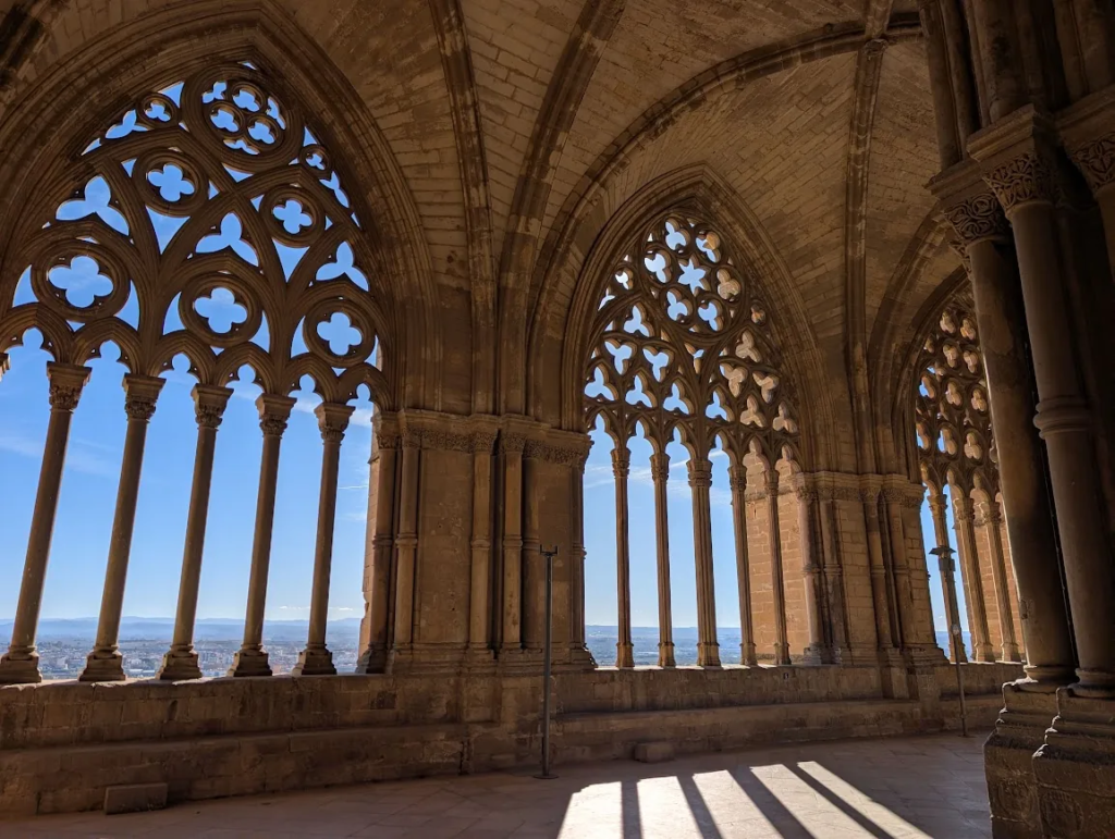 Gothic stone arcade with carved tracery windows at La Seu Vella cathedral in Lleida, Spain, overlooking the city and distant hills