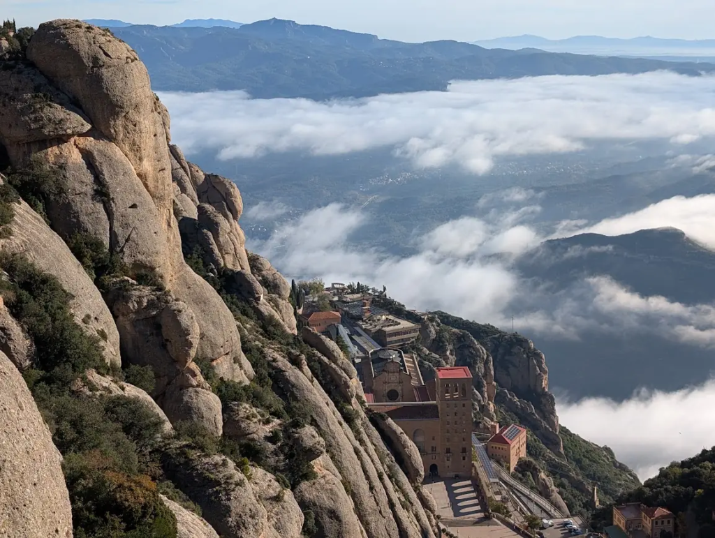 View from a hiking trail near Montserrat, jagged rock formations in the foreground and clouds filling the valley below