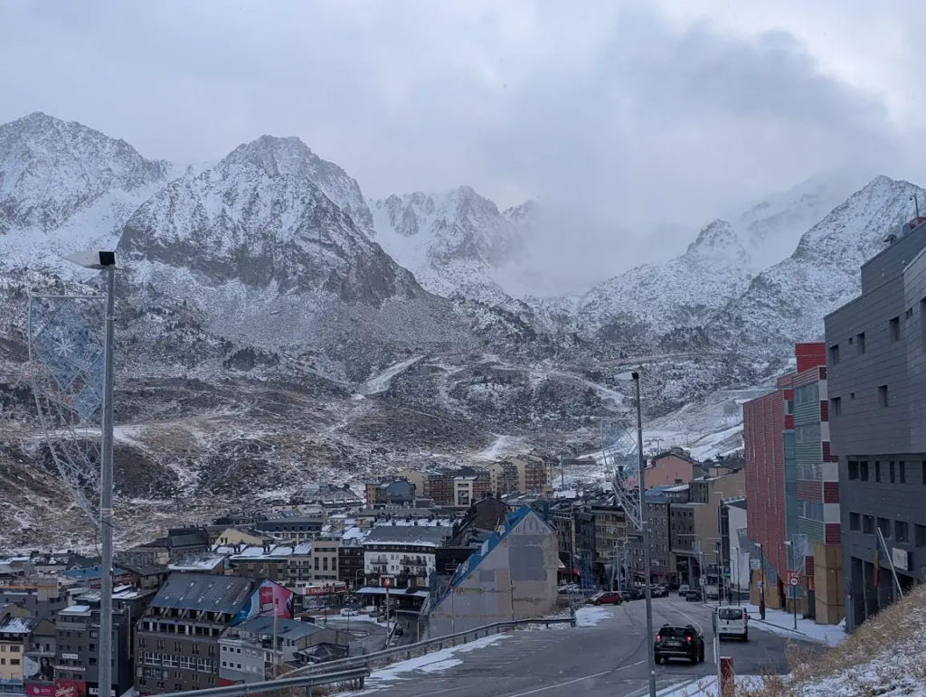 Snow-covered mountains above the town of Pas de la Casa in Andorra in late November, with a road and apartment buildings in the foreground