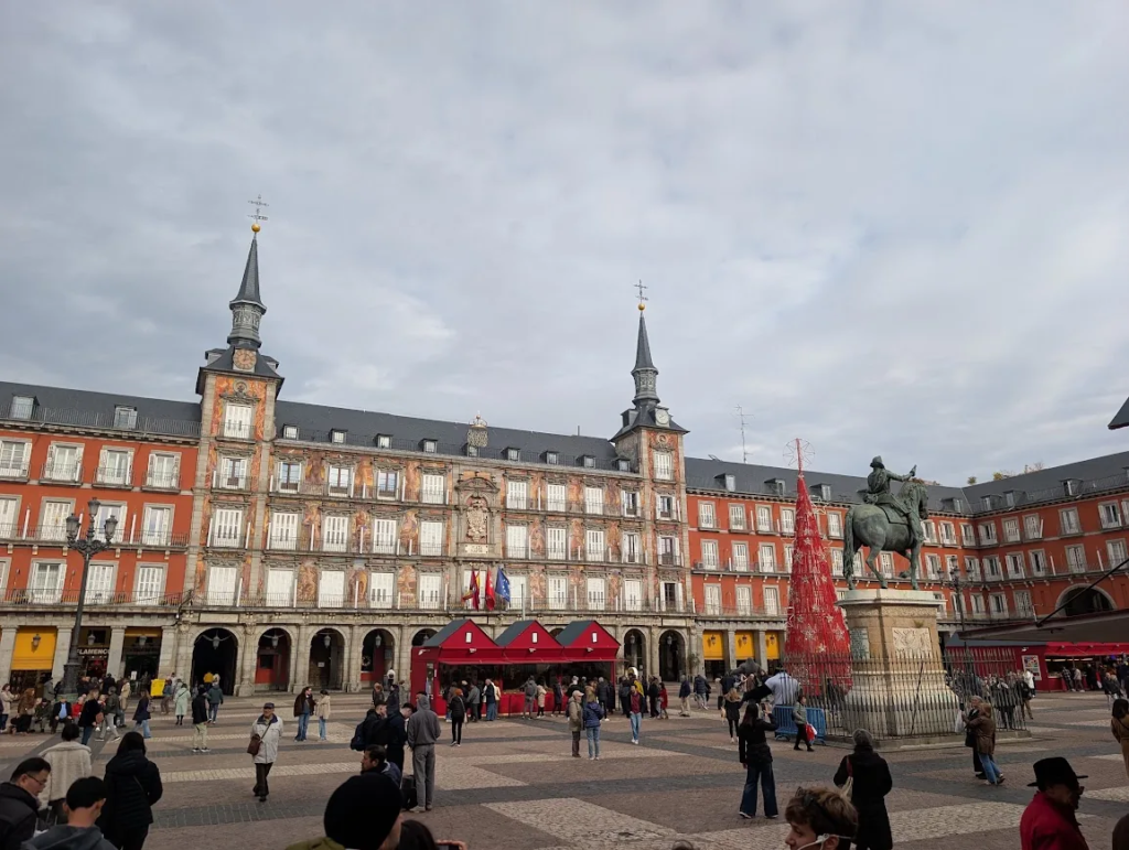 Plaza Mayor in Madrid, Spain, with red Christmas market stalls, a tall red tree and the equestrian statue of Philip III in the square