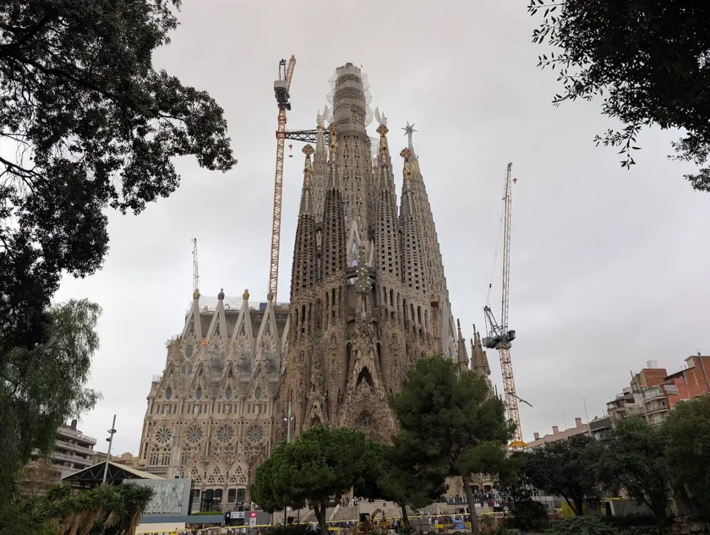 Sagrada Familia exterior in Barcelona, Gaudí's spires with construction cranes still visible, overcast sky