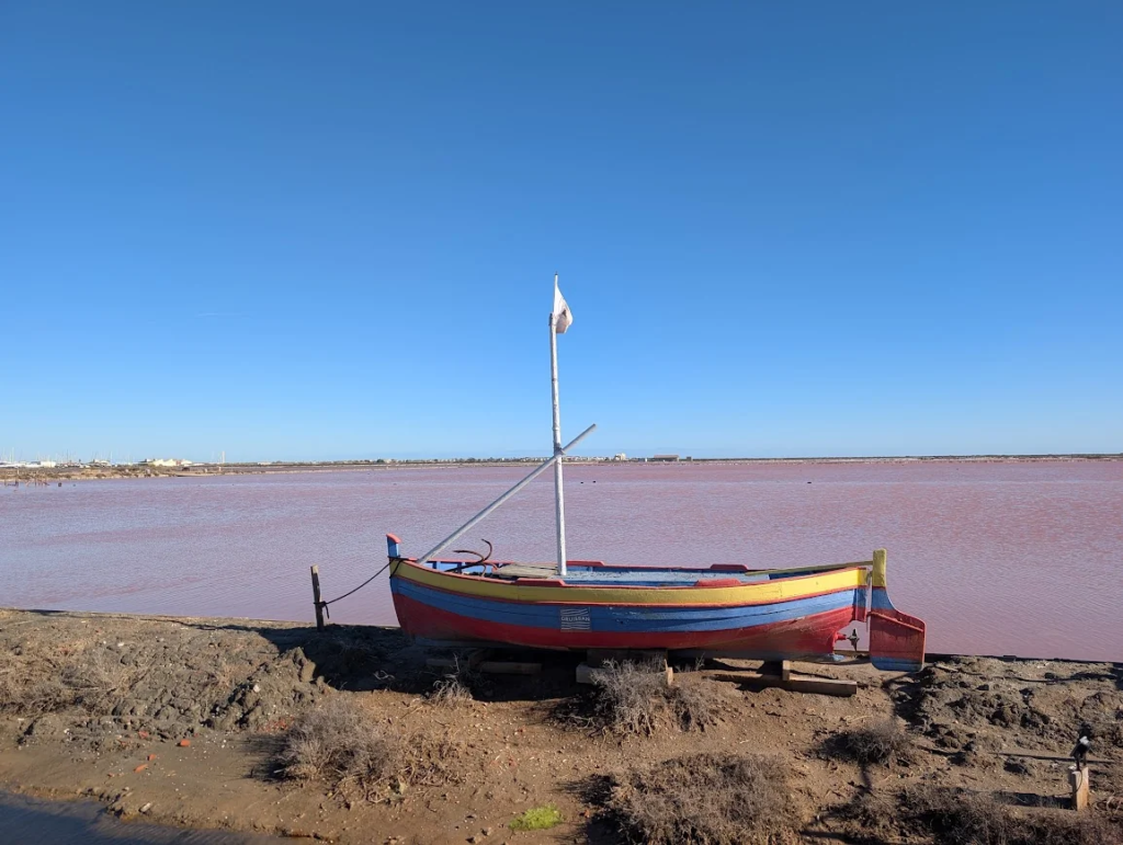 Pink water of the Salins de Gruissan salt marshes near Narbonne with a small colorful wooden boat on the shore