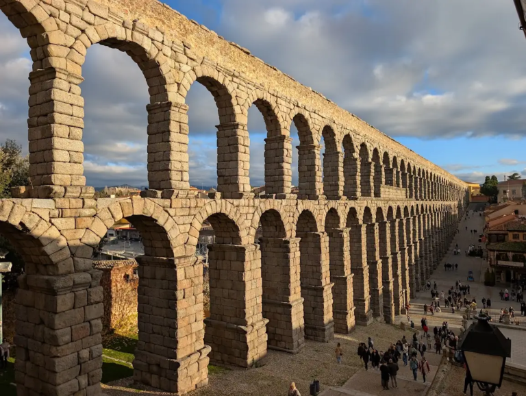 Roman aqueduct in Segovia, Spain, with tourists walking beneath the granite arches in late afternoon light