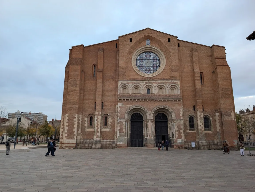 Romanesque brick facade of the Basilica of Saint-Sernin in Toulouse with a rose window and two arched doorways, seen from the square in front