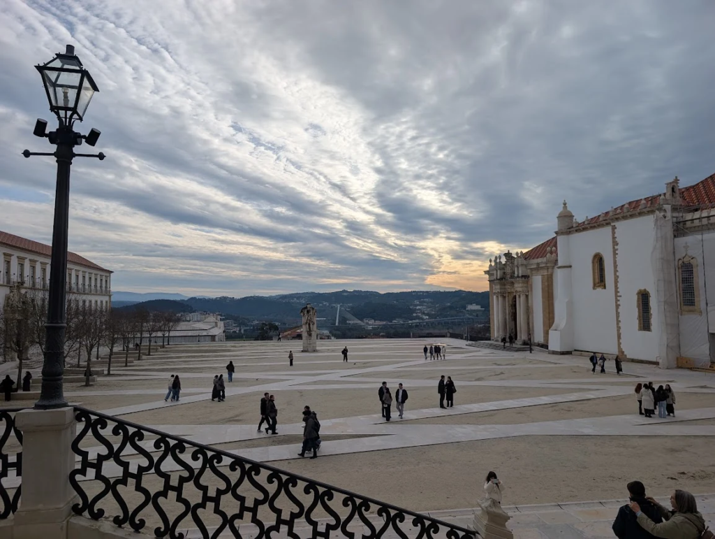 Visitors crossing the courtyard of the Palace of Schools at the University of Coimbra, Portugal, under a cloudy sky