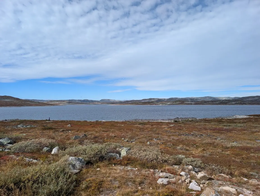Still mountain lake on an empty plateau with autumn-colored tundra under a wide cloudy sky in Norway