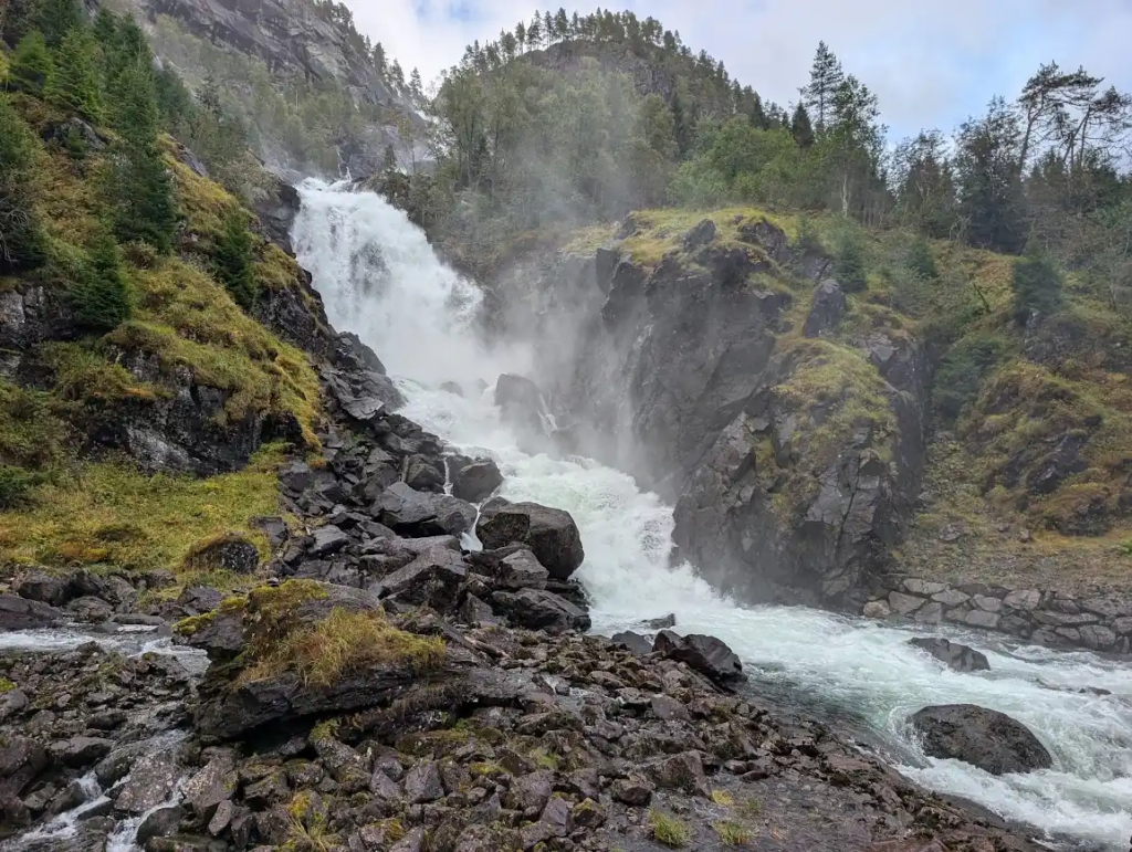Låtefossen waterfall pouring over mossy rocks into a rocky river near Odda in Norway