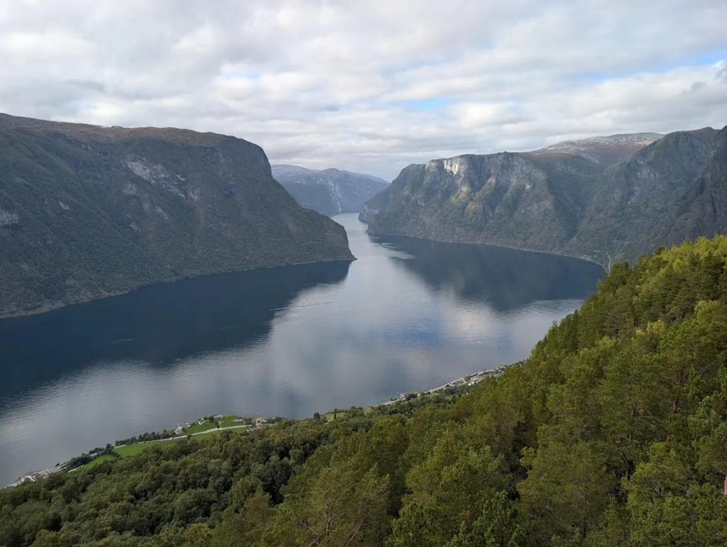 View over the Aurlandsfjord from the Stegastein viewpoint, with steep forested slopes and still water under scattered clouds