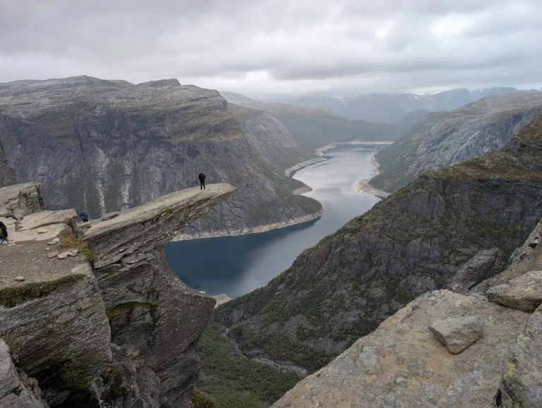 Hiker standing on the Trolltunga rock ledge above Ringedalsvatnet lake on an overcast September day in Norway