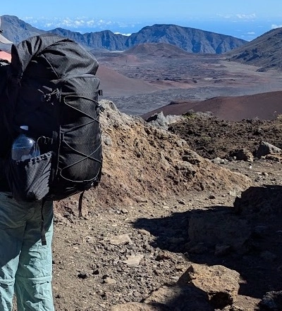 ULA Camino backpack with extended roll-top and a water bottle in the side pocket, worn on a volcanic trail in Haleakalā National Park, Maui
