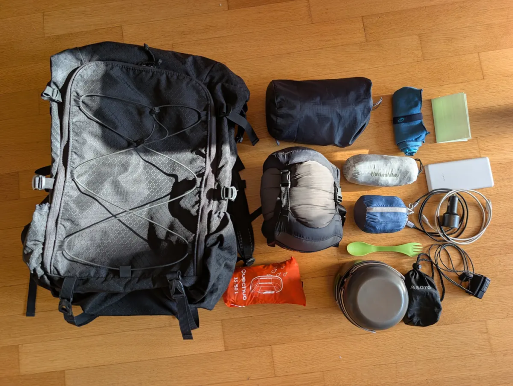 Complete 3.8kg ultralight backpacking gear flat lay on a hardwood floor next to a black ULA Camino backpack, showing sleeping gear, cookset, power banks, and accessories.